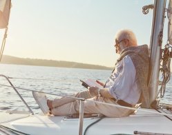 hombre-senior-relajado-leyendo-libro-mientras-sentado-costado-barco-vela-o-cubierta-yate-flotando_386185-1007